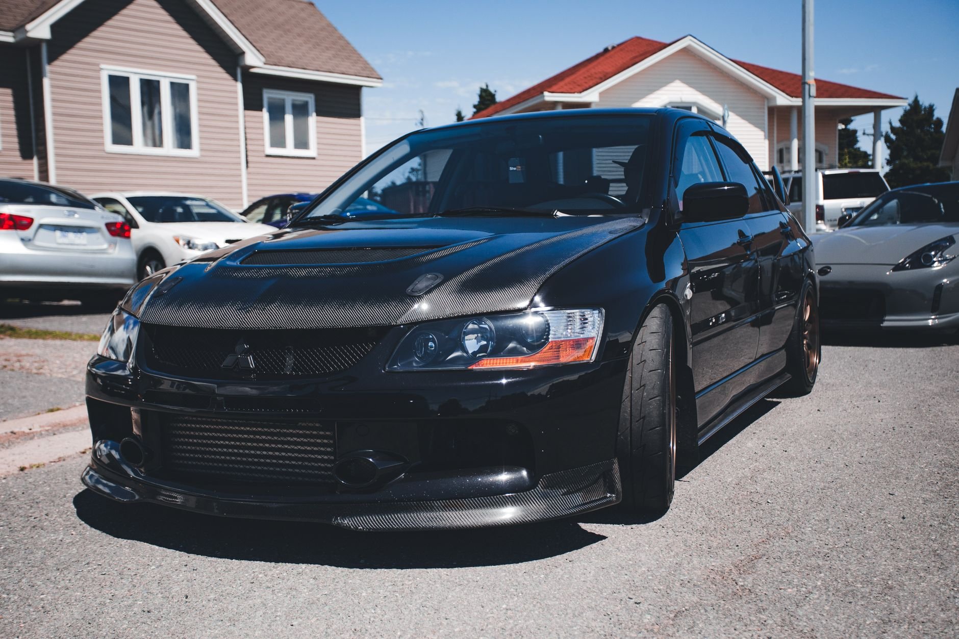 A shiny black sports car parked on a suburban street amidst houses and other vehicles.